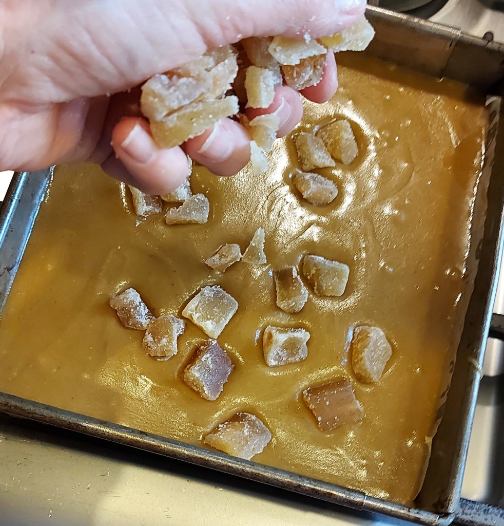 A baking tray filled with oat and ginger slice, with the final addition of crystalised ginger.