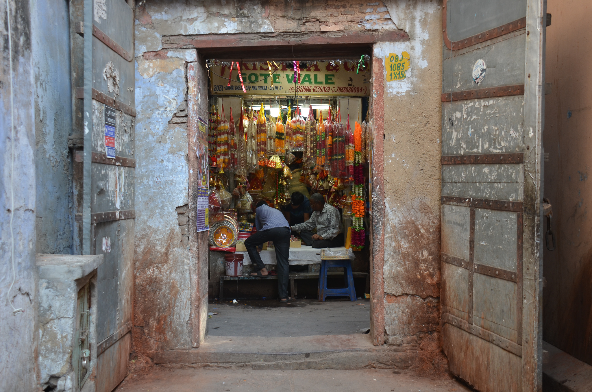 View of a colorful shop in Old Delhi, showcasing various decorative items and flowers, with people interacting inside.