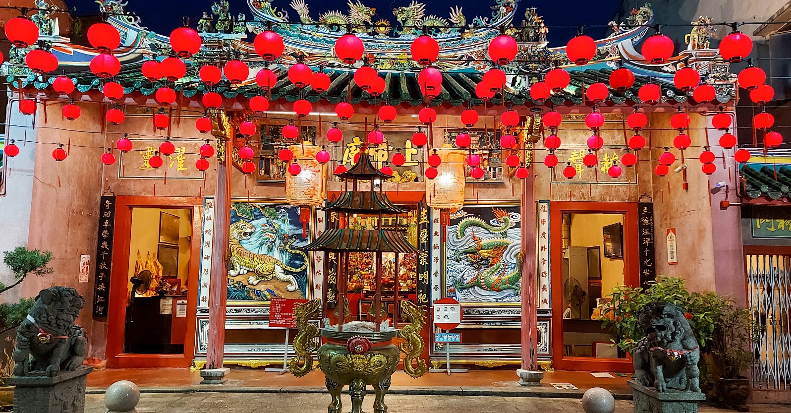 Entrance to a Chinese temple adorned with red lanterns and intricate decorations, set against a night sky.