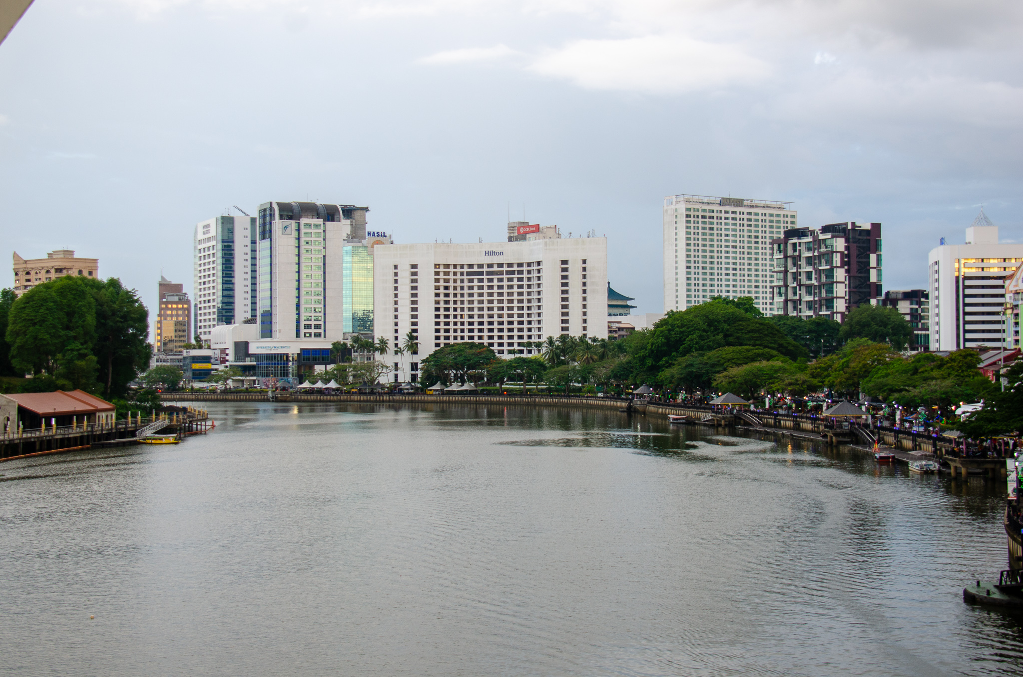 View of Kuching Waterfront with modern buildings and lush trees alongside the river