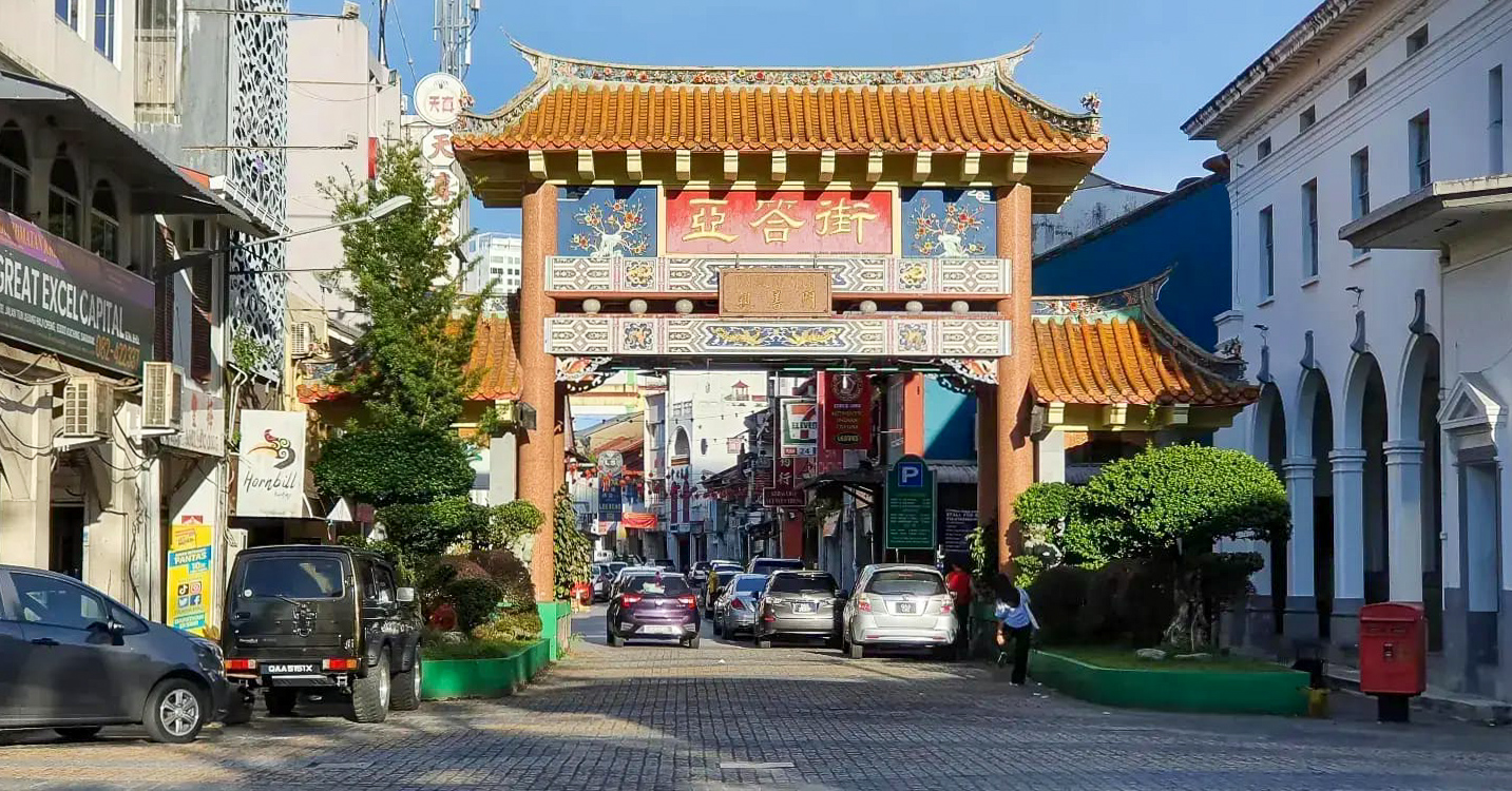 Entrance to Carpenter Street featuring a colorful traditional Chinese archway with surrounding buildings and vehicles.