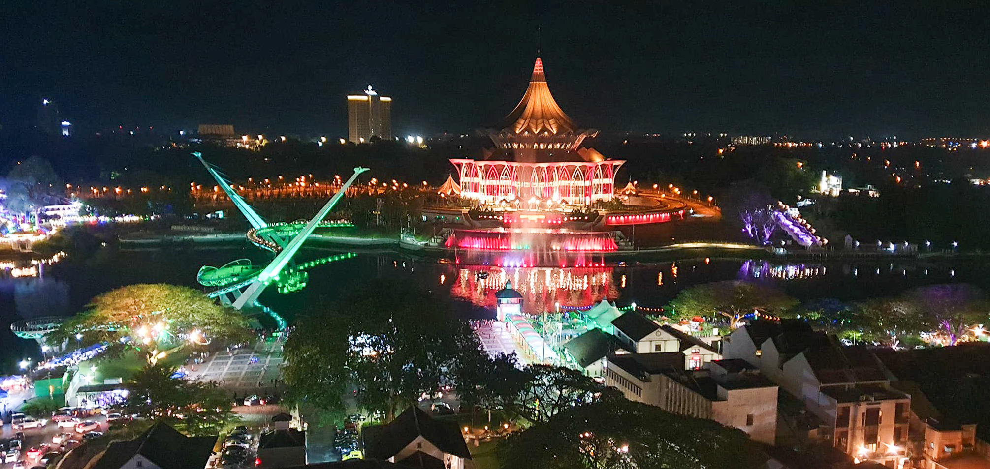 Night view of Kuching showing colorful lights, the waterfront area, and the iconic Sarawak's State Assembly Building.
