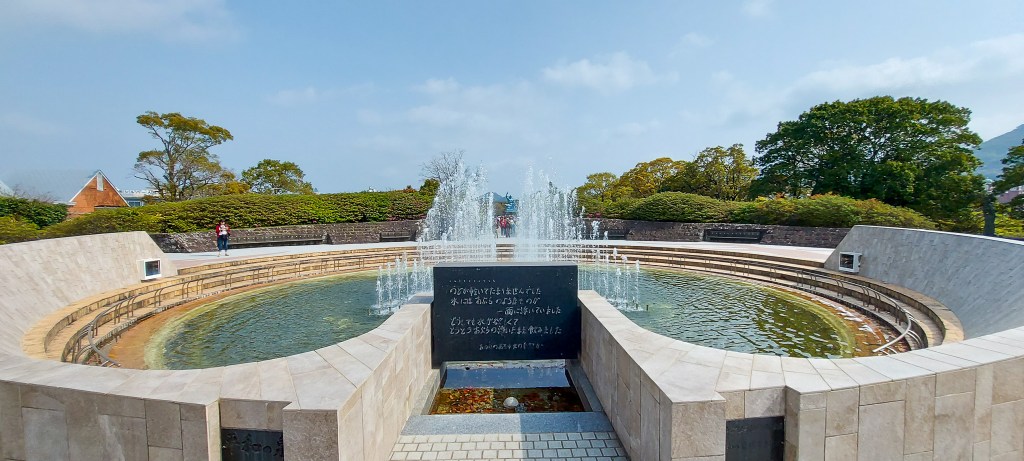 A serene park featuring a circular water fountain surrounded by neatly landscaped greenery and stone pathways.