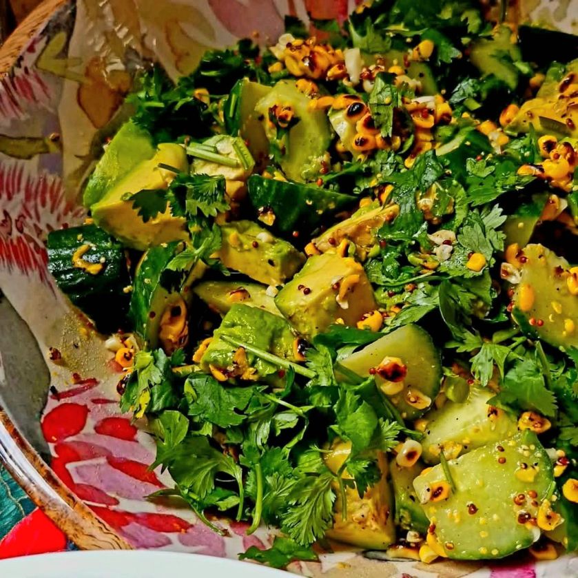 A vibrant salad of charred sweetcorn, creamy avocado chunks, fresh herbs, and diced red onion, served in a bowl with a light citrus dressing.