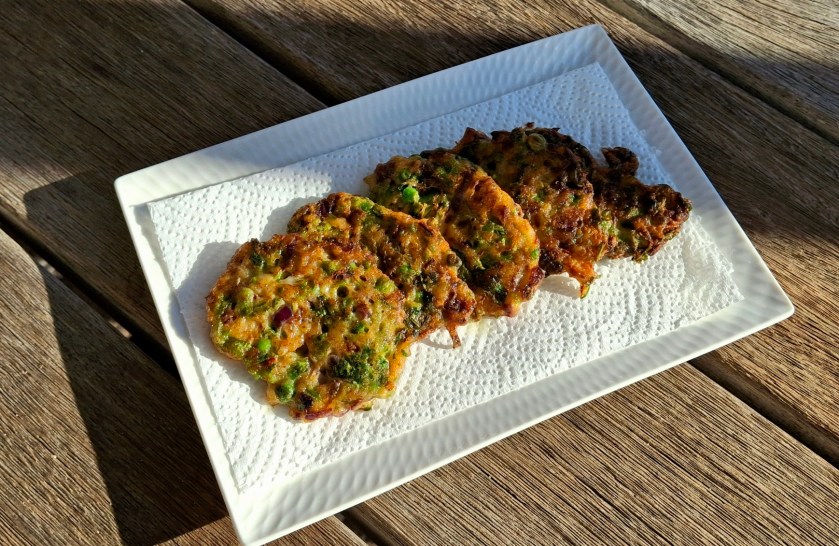 Four crispy Thai prawn fritters arranged on a white serving dish, golden and textured with visible herbs and spices.