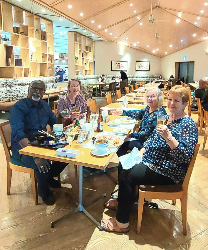 A group of four friends enjoying a meal together in a cozy restaurant, raising their glasses in a toast. The table is set with various dishes and drinks, and the warm ambiance is complemented by soft lighting and wooden decor.