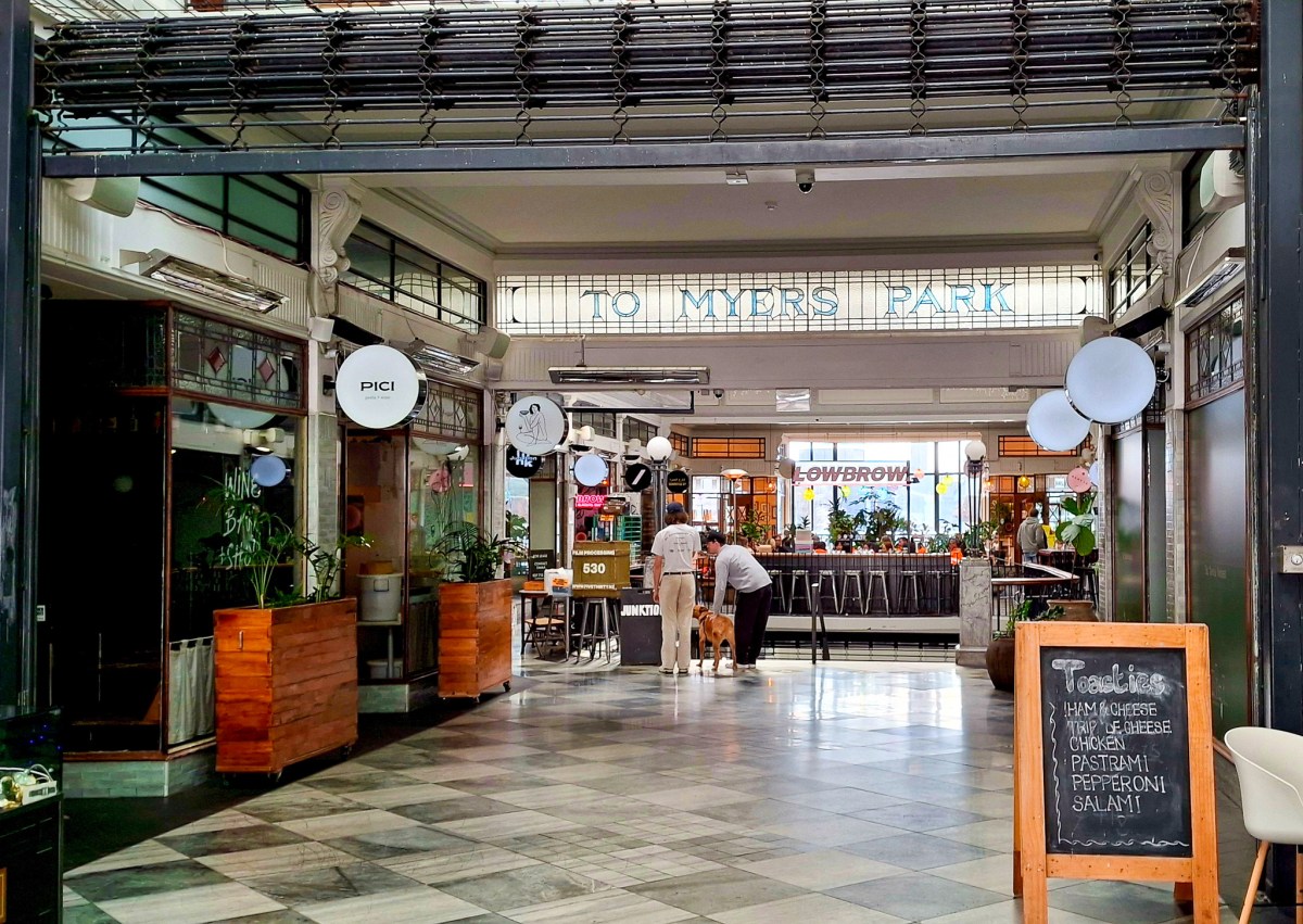 Interior view of a passageway leading to Myers Park, featuring various eateries and a busy atmosphere.