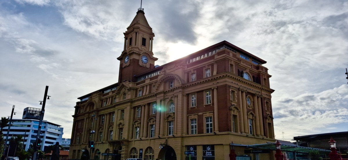 Historic building with a clock tower and ornate architecture, illuminated by sunlight against a cloudy sky.