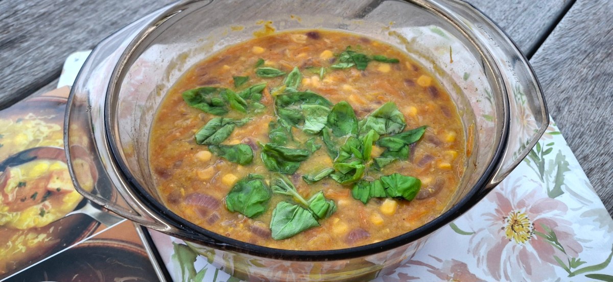 A glass casserole dish filled with sweetcorn chowder topped with fresh basil leaves, sitting on a floral-patterned kitchen towel.