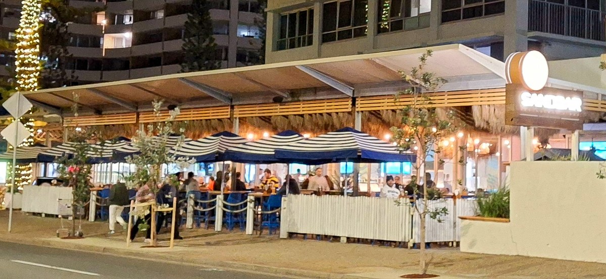 Outdoor view of Sandbar restaurant at night with striped awnings, trees, and patrons dining.