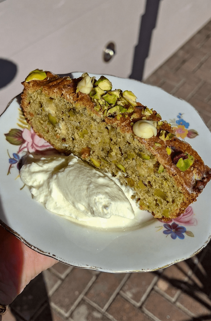 Slice of pistachio cake with cream on a floral plate held by a hand