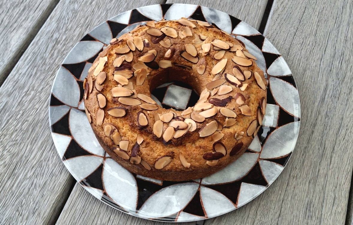 Classic Almond Cake Recipe Round almond cake with sliced almonds on a patterned plate placed on a wooden surface